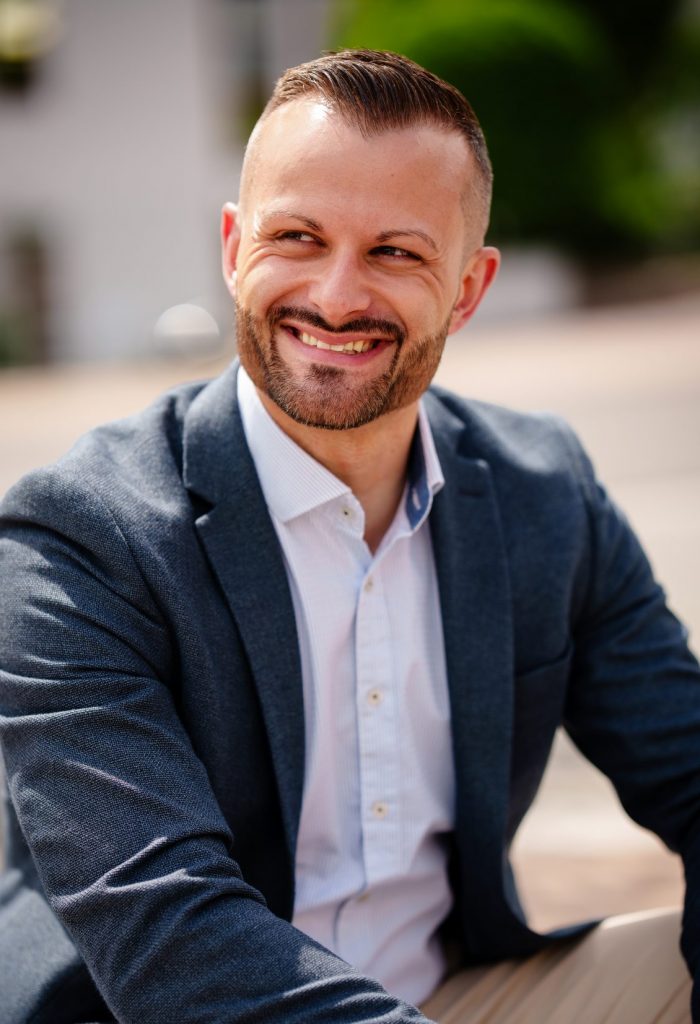 Person sitting outdoors smiling sideways.